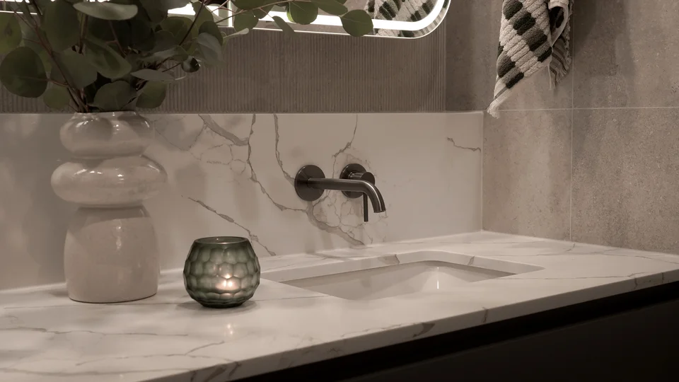 Marble bathroom vanity with a wall-mounted tap, vase and candle.