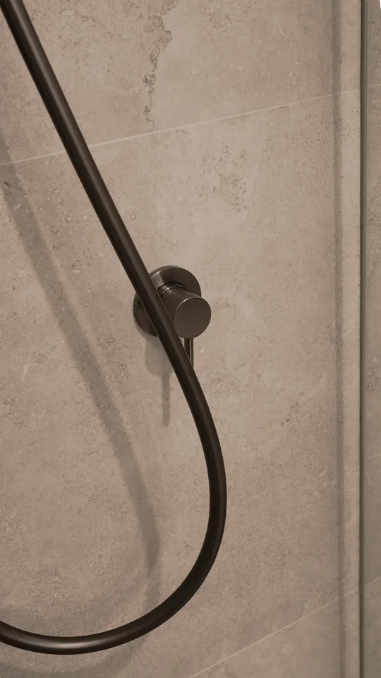 Handheld shower fitting against a textured neutral wall.