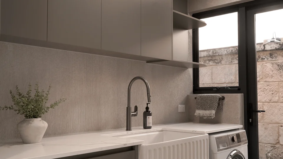 Light stone sink and dark tap beneath fitted cabinets and a window.