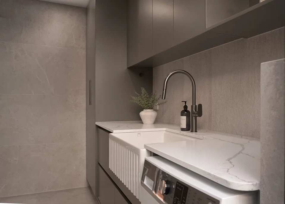 Light stone sink and dark tap beneath fitted cabinets and a window.