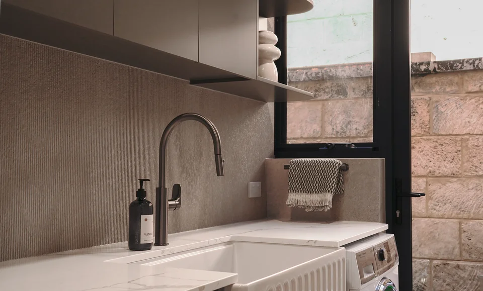 Light stone sink and dark tap beneath fitted cabinets and a window.