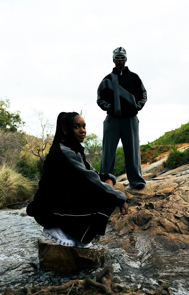 Models wearing black and grey outerwear among rocks and trees.
