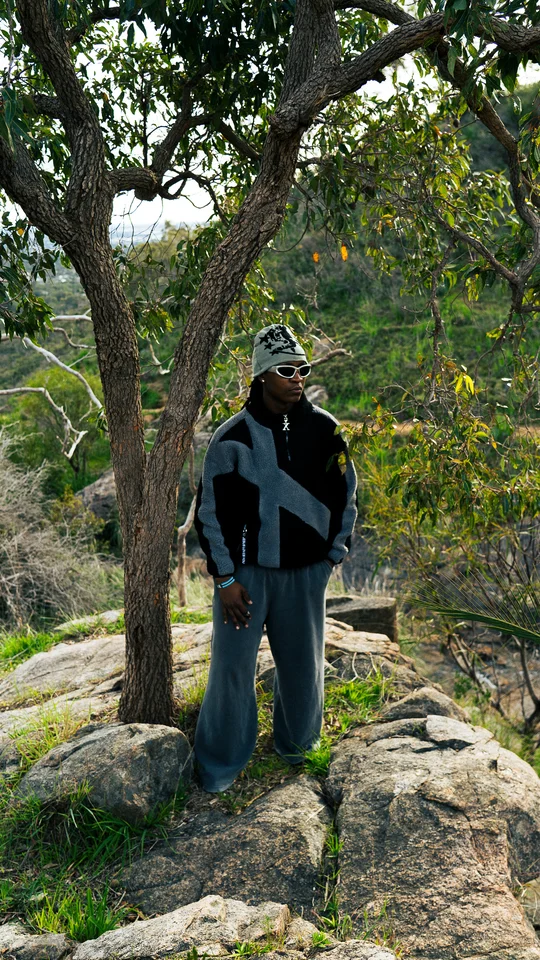 Models wearing black and grey outerwear among rocks and trees.
