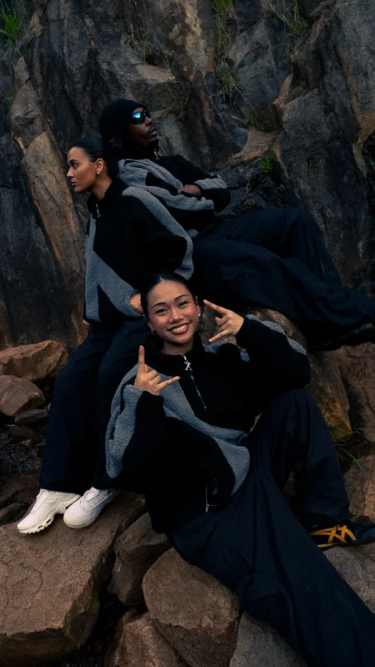 Models in dark outerwear seated together on rocks.