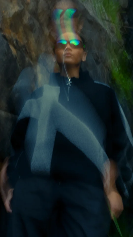 Motion-blurred portrait of a model in dark outerwear against rocks.