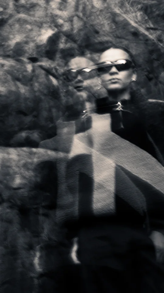 Motion-blurred portrait of a model in dark outerwear against rocks.