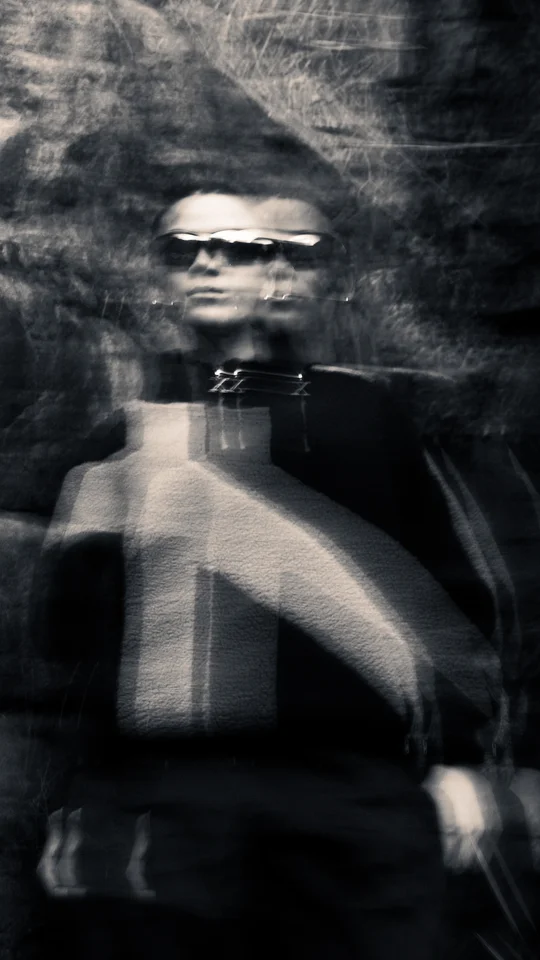 Motion-blurred portrait of a model in dark outerwear against rocks.