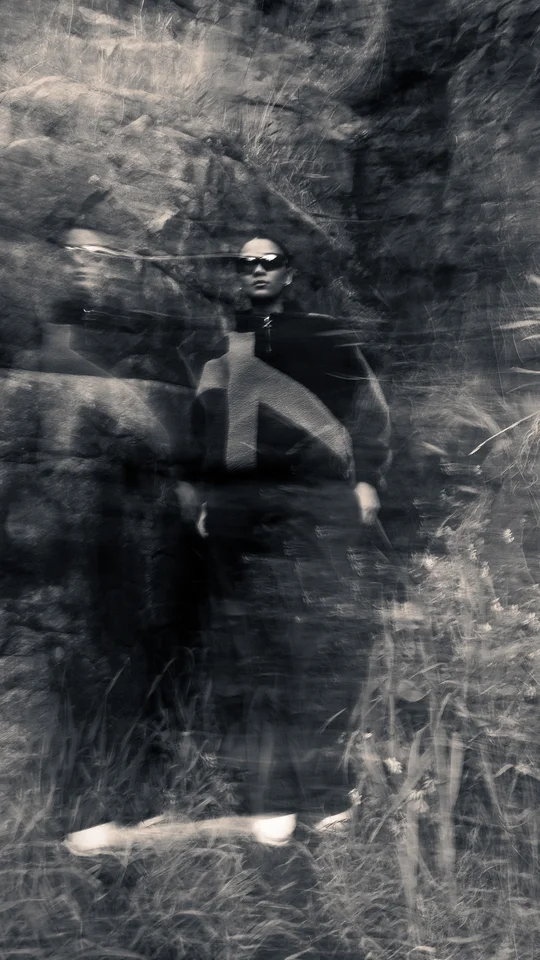 Motion-blurred portrait of a model in dark outerwear against rocks.