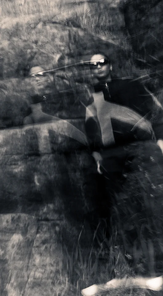 Motion-blurred portrait of a model in dark outerwear against rocks.