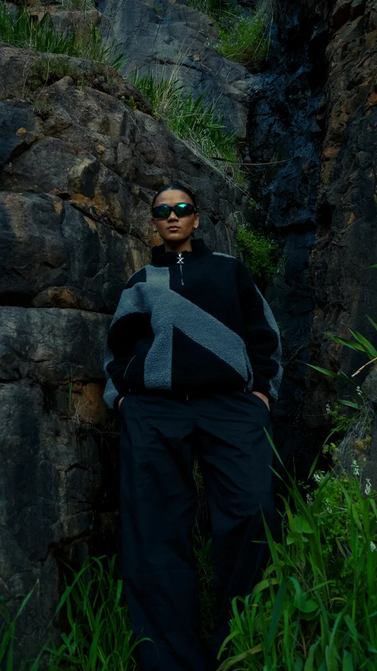Model in black and grey outerwear standing against a rock face.