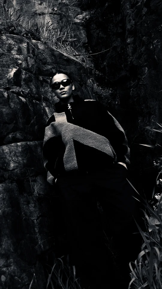 Model in black and grey outerwear standing against a rock face.