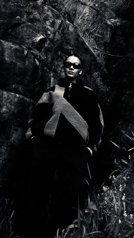Model in black and grey outerwear standing against a rock face.