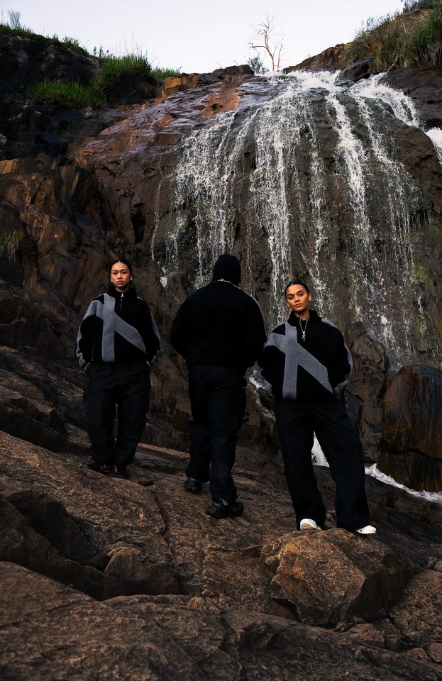 Models standing on rocks in front of a waterfall.