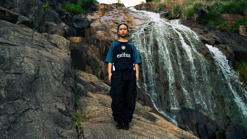 Model wearing a dark graphic T-shirt in front of a waterfall.