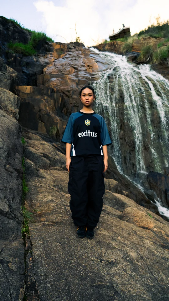 Model wearing a dark graphic T-shirt in front of a waterfall.