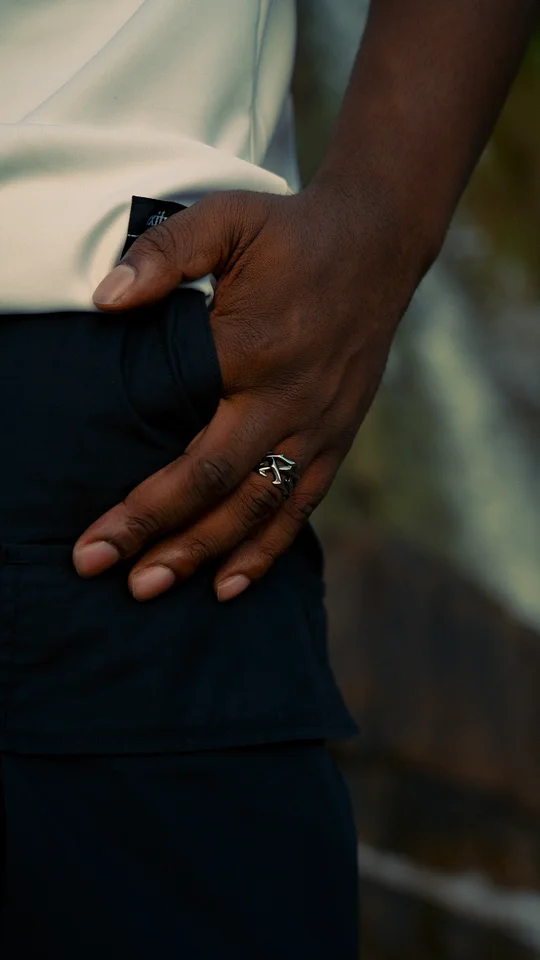 Close-up of a hand wearing a silver ring beside dark trousers.