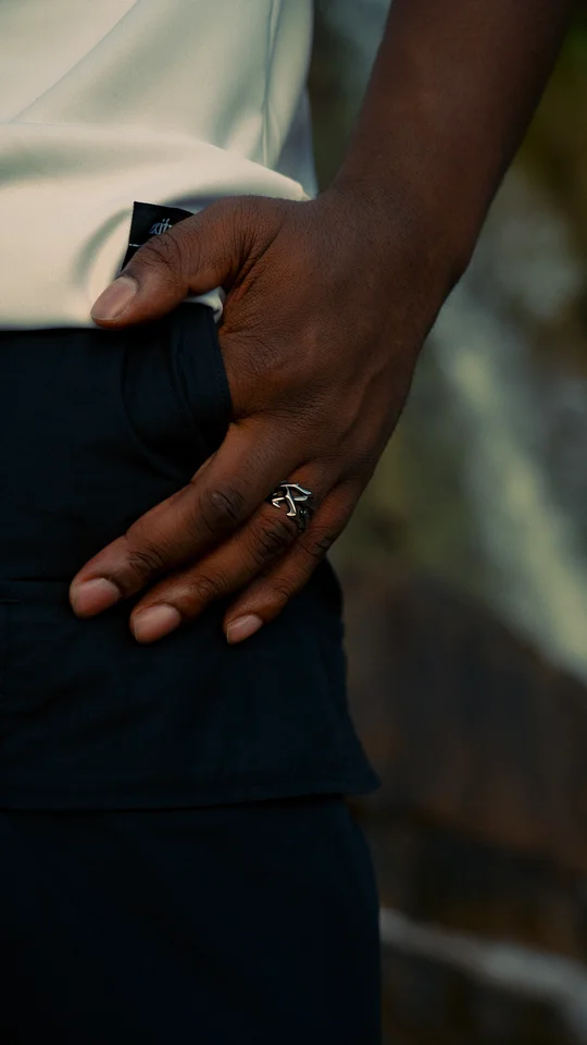 Close-up of a hand wearing a silver ring beside dark trousers.