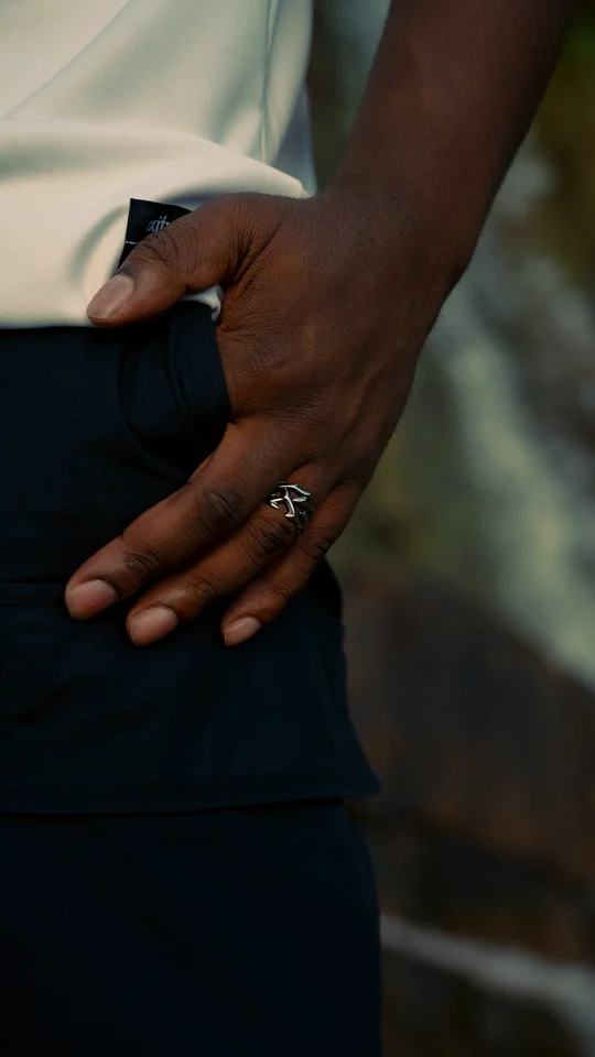 Close-up of a hand wearing a silver ring beside dark trousers.