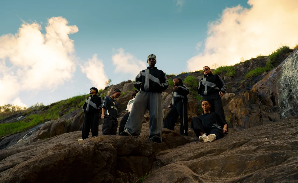 Models in black and grey clothing on a rocky hillside under open sky.