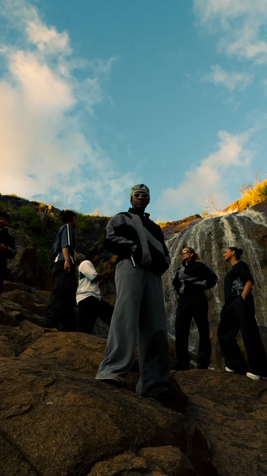 Models in black and grey clothing on a rocky hillside under open sky.
