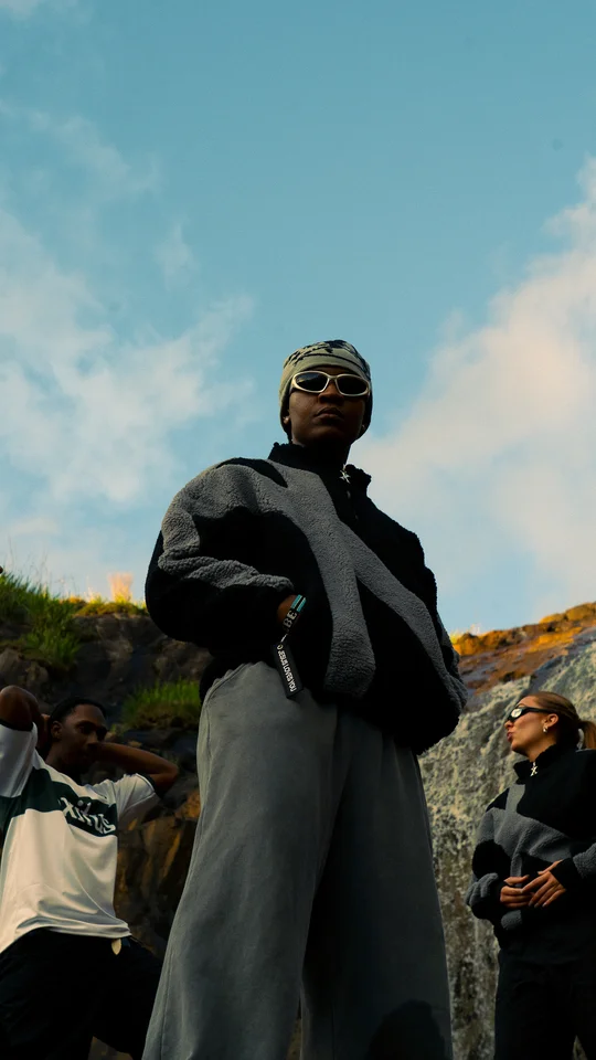 Models in black and grey clothing on a rocky hillside under open sky.