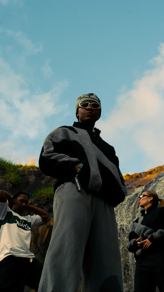 Models in black and grey clothing on a rocky hillside under open sky.
