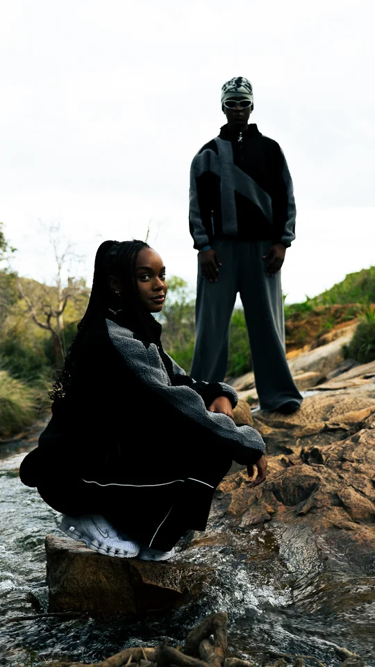 Two models in black and grey outerwear posed on rocks.