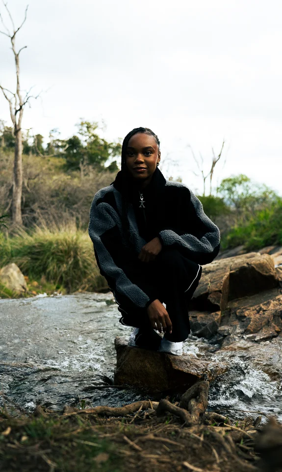 Model crouching on rocks in a black and grey jacket.