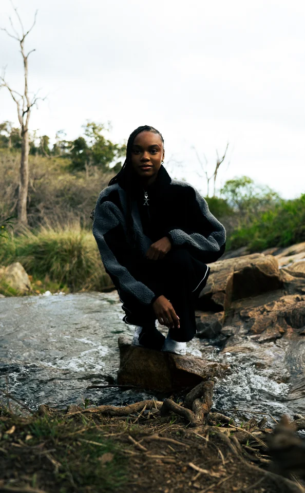 Model crouching on rocks in a black and grey jacket.
