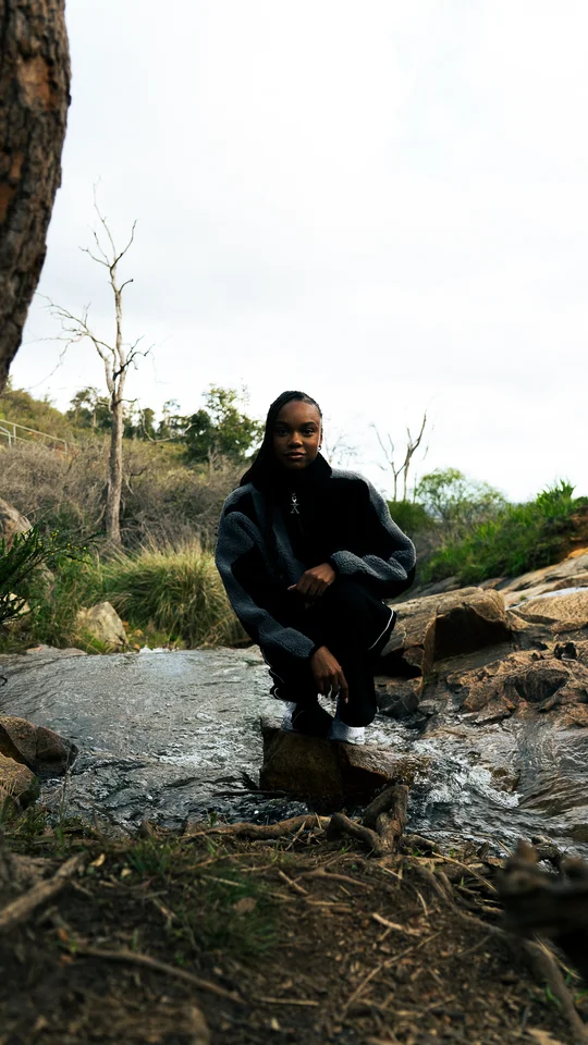 Model crouching on rocks in a black and grey jacket.