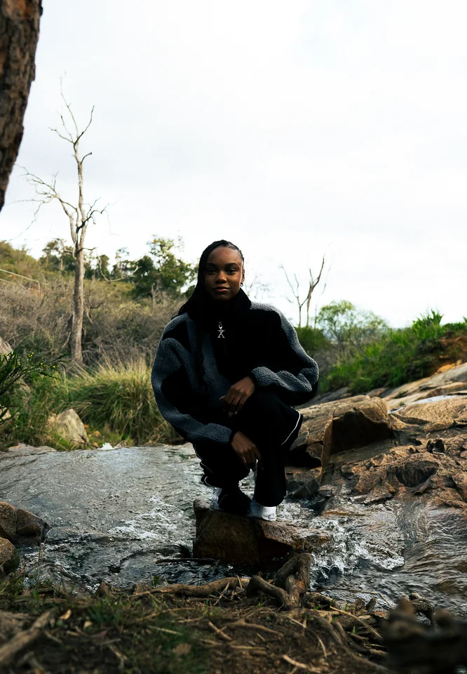 Model crouching on rocks in a black and grey jacket.