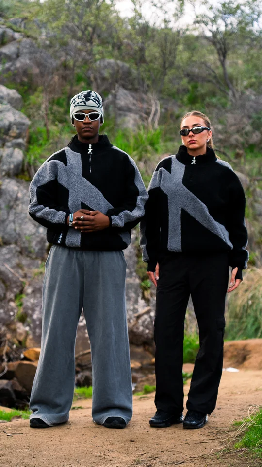 Two models wearing coordinated black and grey jackets outdoors.