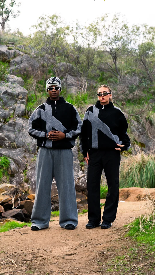 Two models wearing coordinated black and grey jackets outdoors.