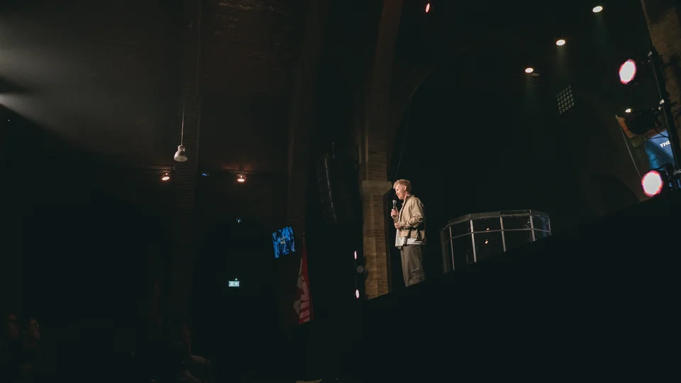 Performer holding a microphone on a dimly lit stage.