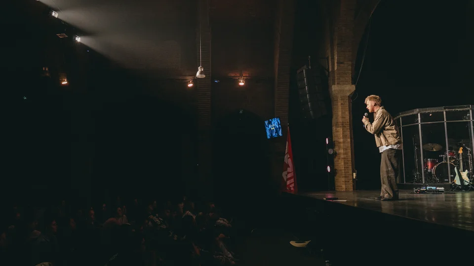 Performer holding a microphone on a dimly lit stage.