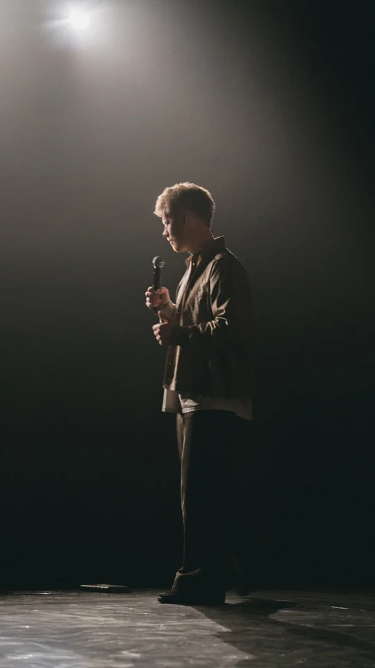 Performer holding a microphone on a dimly lit stage.