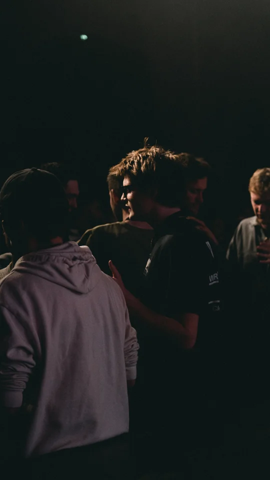 People talking in the shadows beside a live stage.