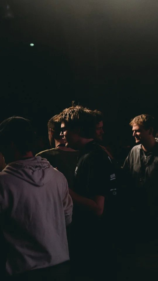 People talking in the shadows beside a live stage.