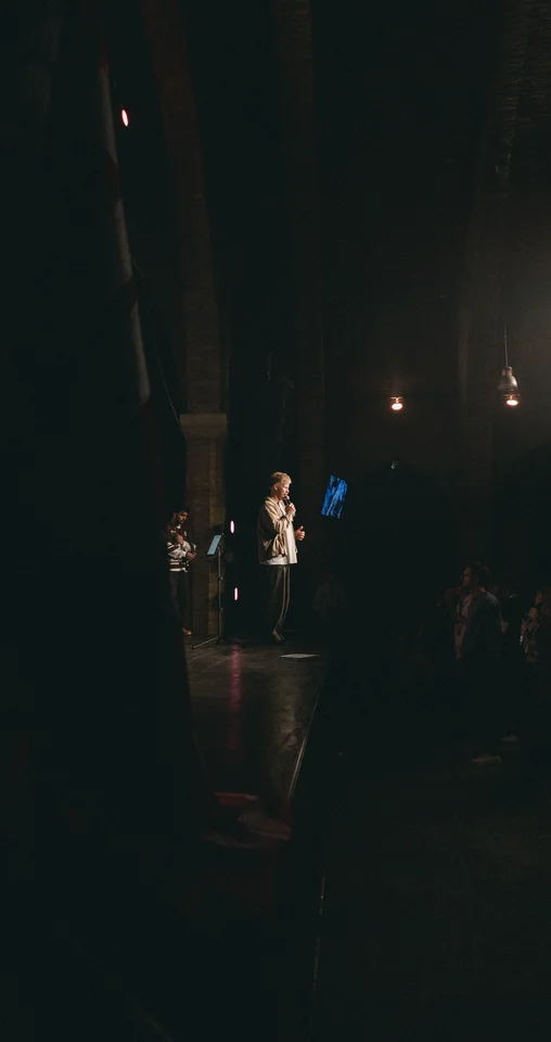 View from the side of the stage toward a performer and the audience.