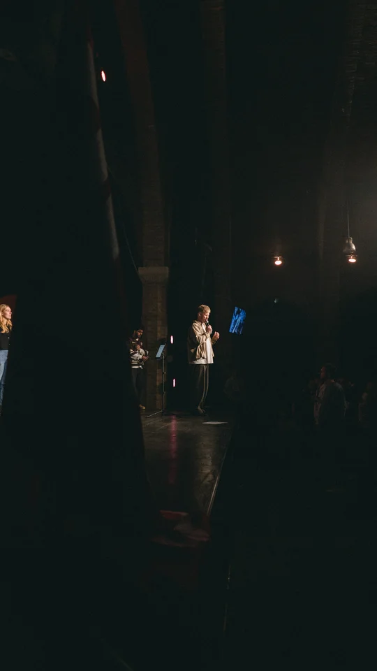View from the side of the stage toward a performer and the audience.