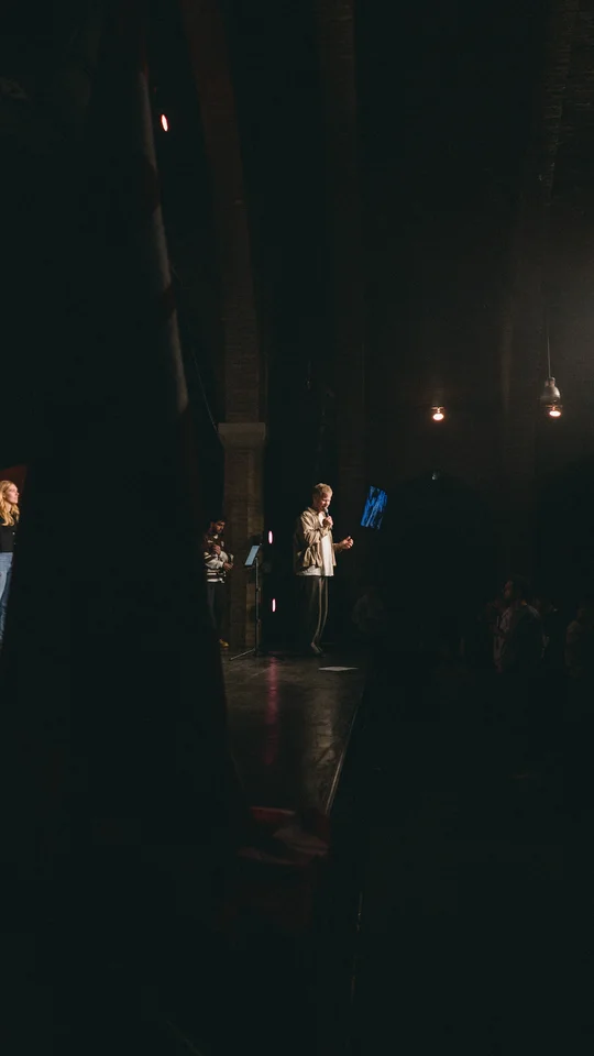 View from the side of the stage toward a performer and the audience.