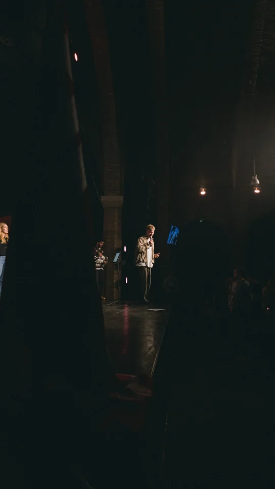 View from the side of the stage toward a performer and the audience.