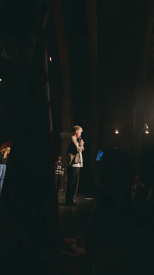 View from the side of the stage toward a performer and the audience.