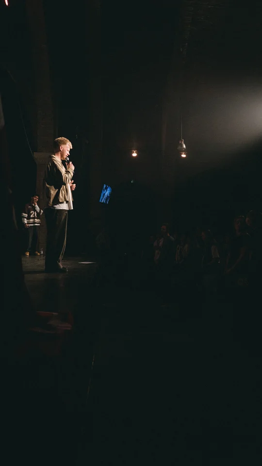 View from the side of the stage toward a performer and the audience.